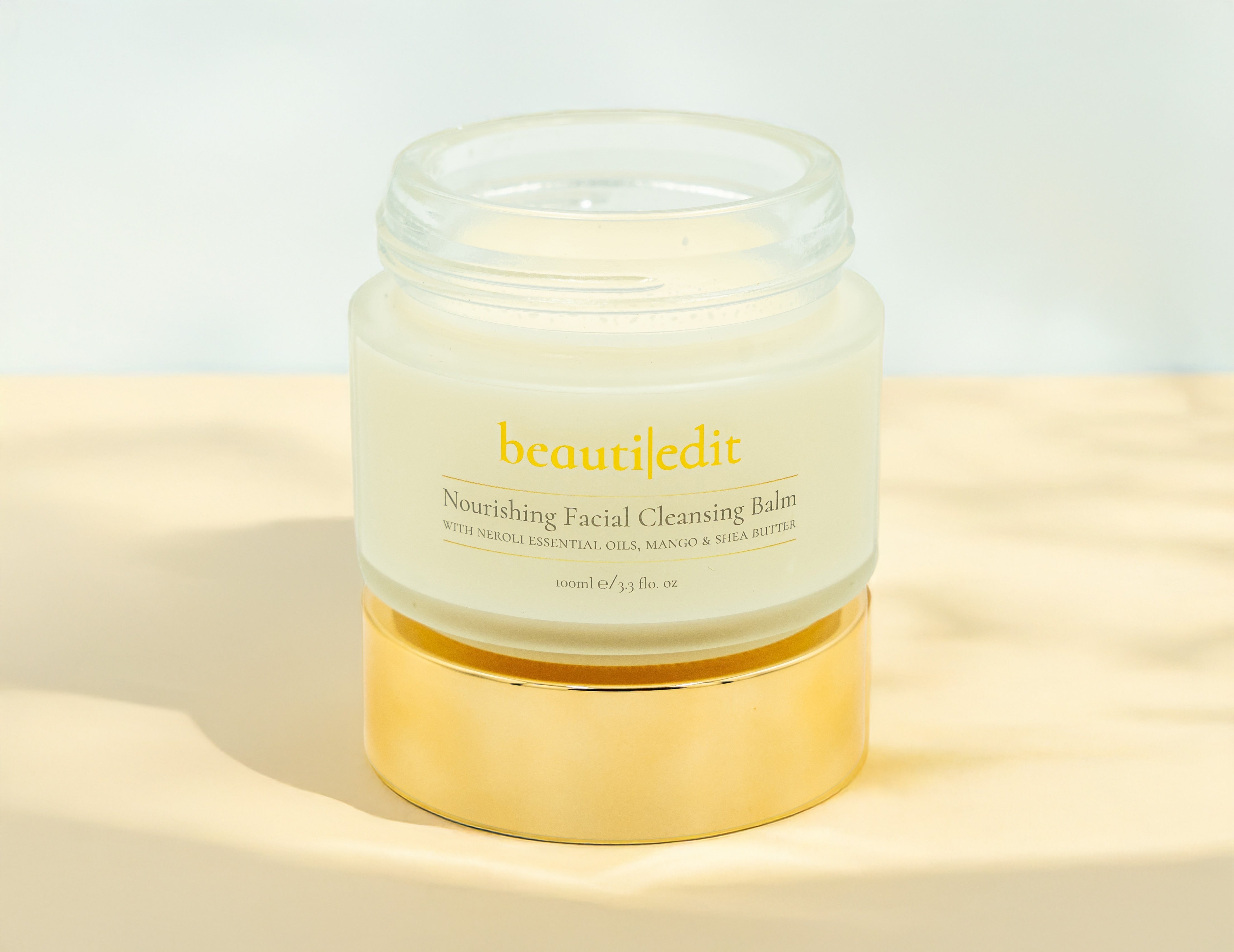 Open BeautiEdit Facial Cleansing Balm sitting on the gold lid. Background is sandy.