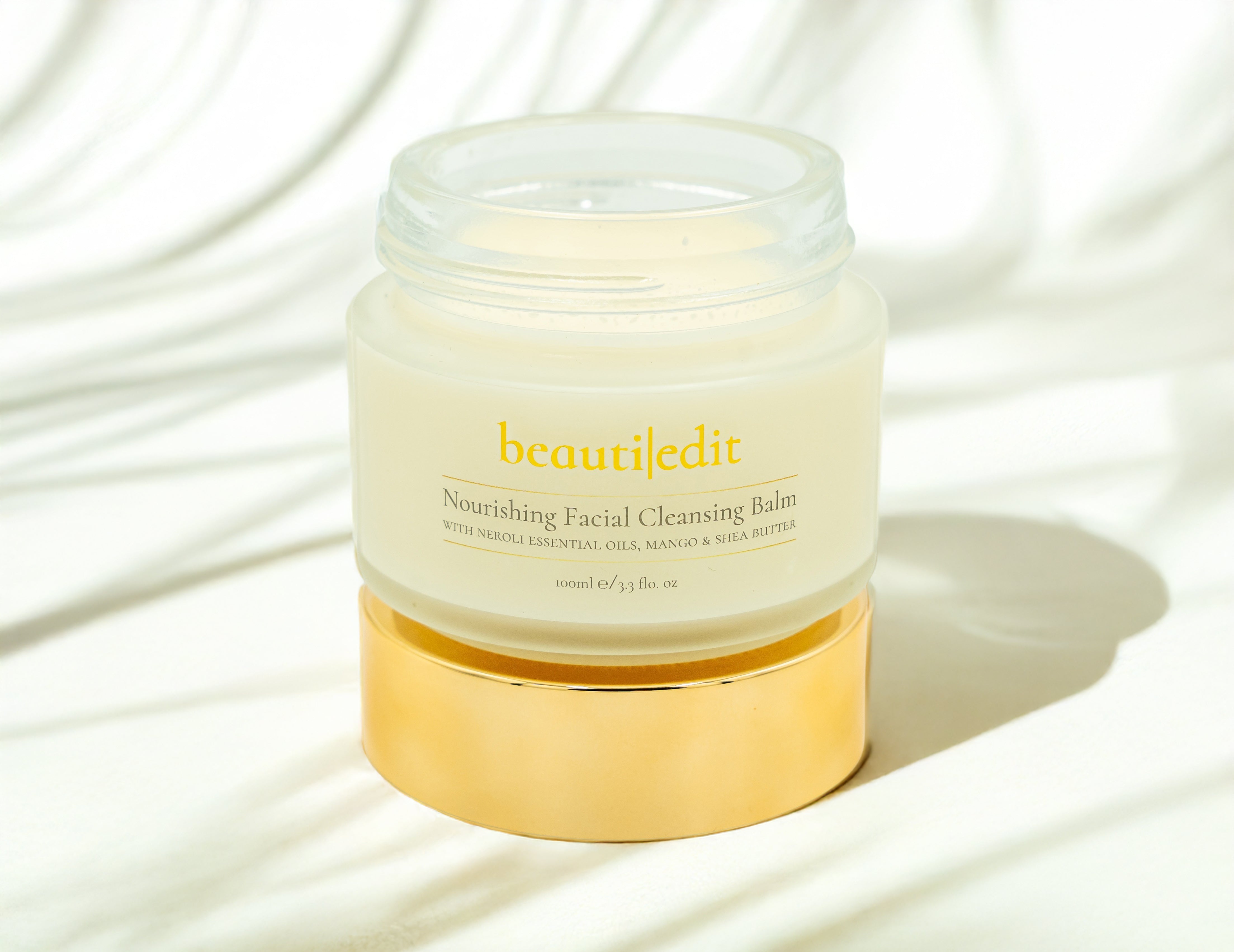 Open BeautiEdit Facial Cleansing Balm sitting on the gold lid. Background has striped shadows.